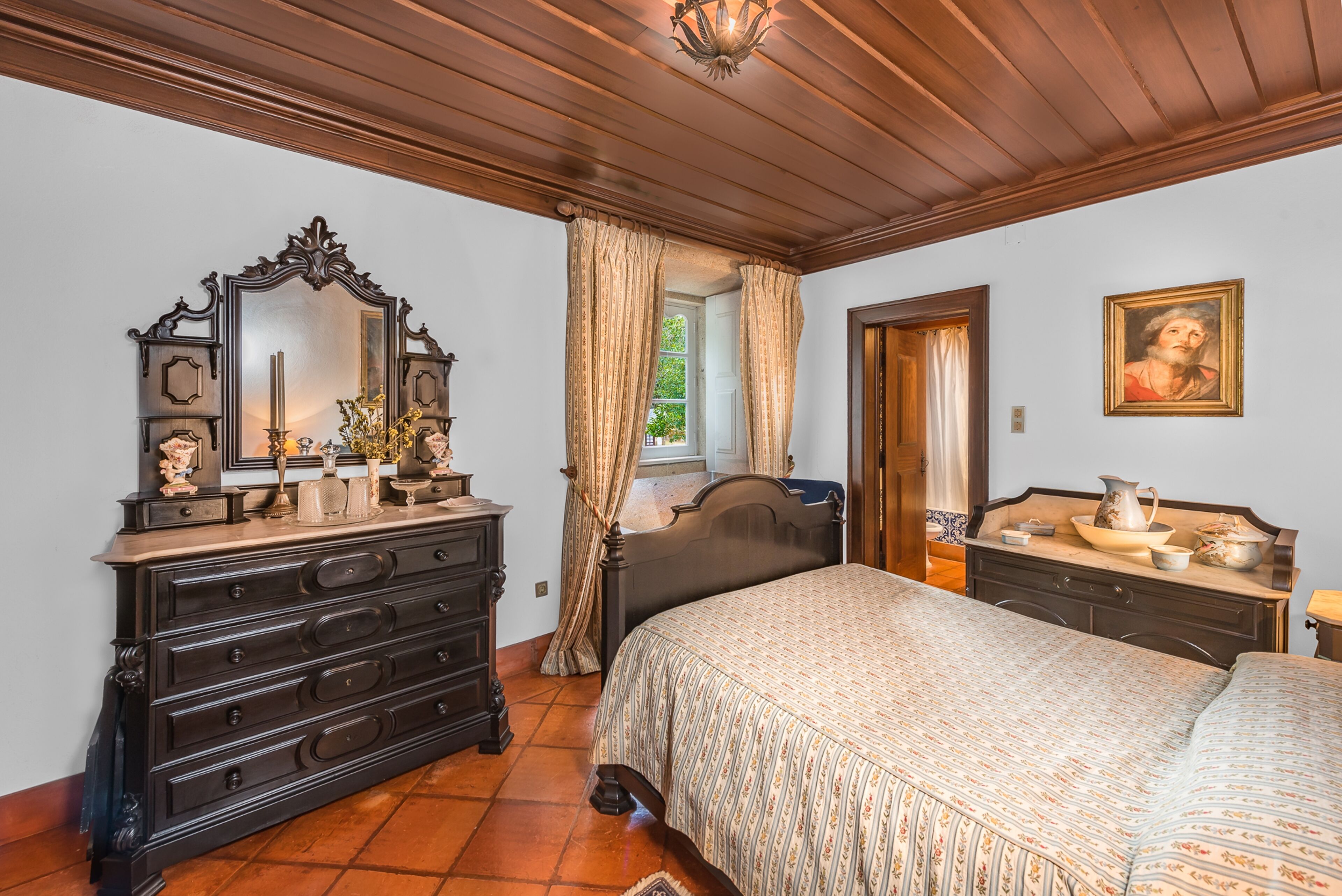 Quarto com uma cama grande, penteadeira, espelho e uma porta que dá para outro cômodo.