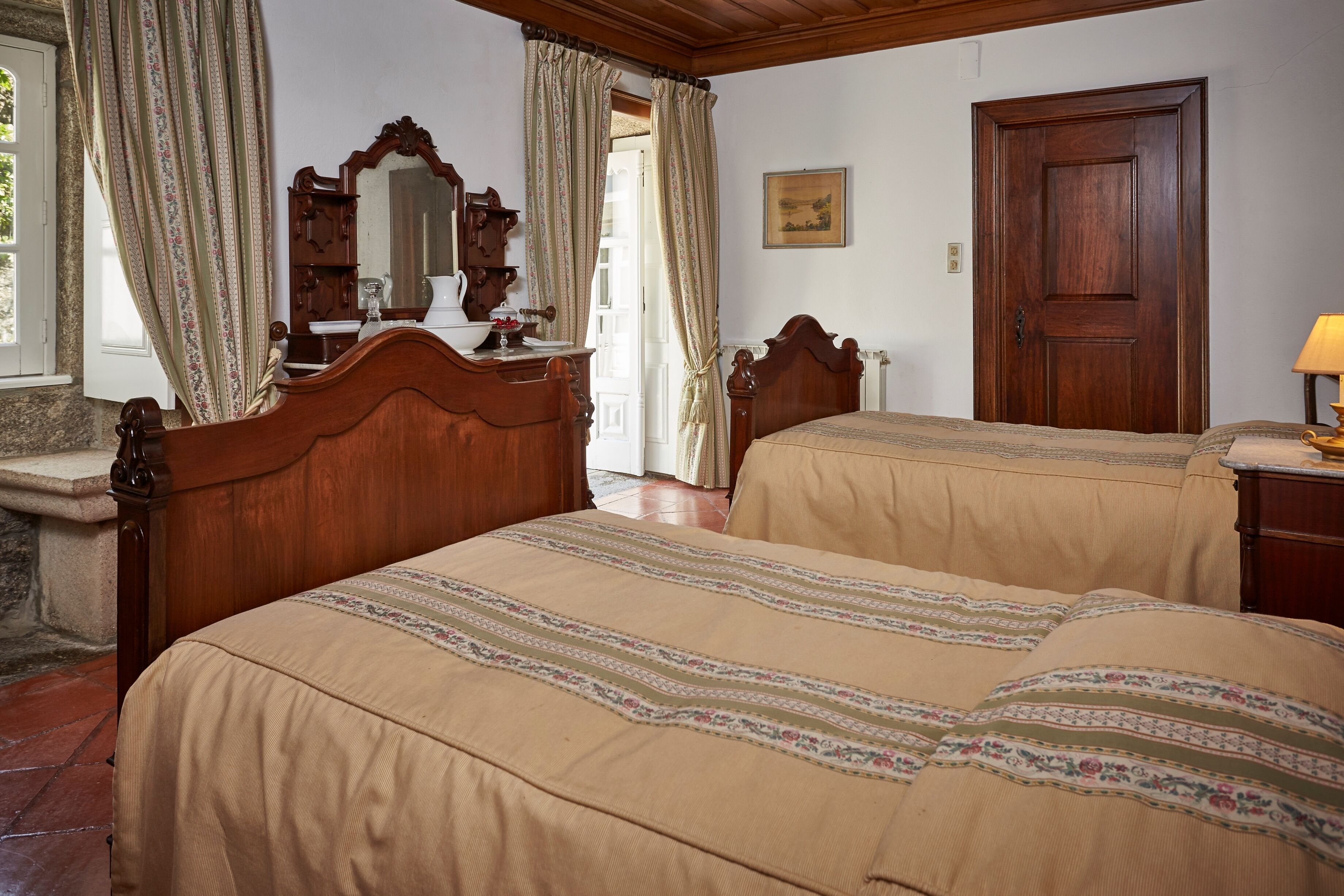 A bedroom with two wooden beds, a dresser, a mirror, and a door.