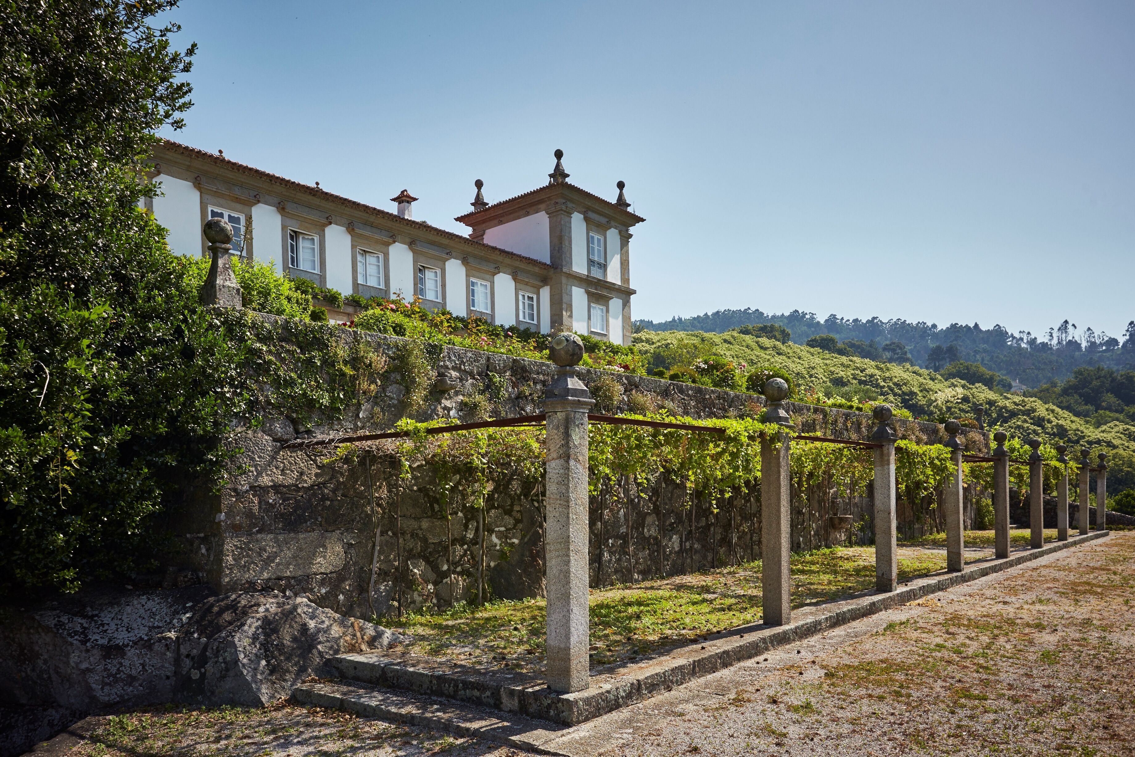 A historic building with a stone wall and a vine-covered trellis.