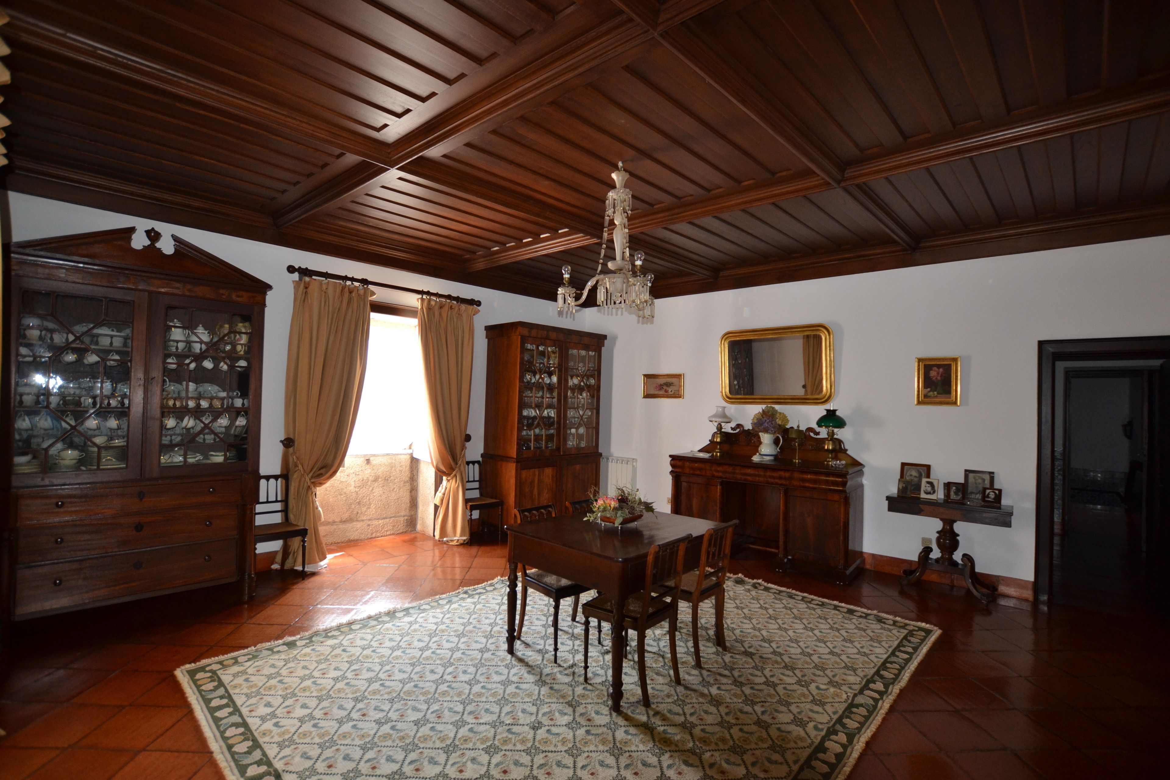 A dining room with a wooden table, chairs, and a chandelier. There is a cabinet with glass doors and a mirror on the wall.