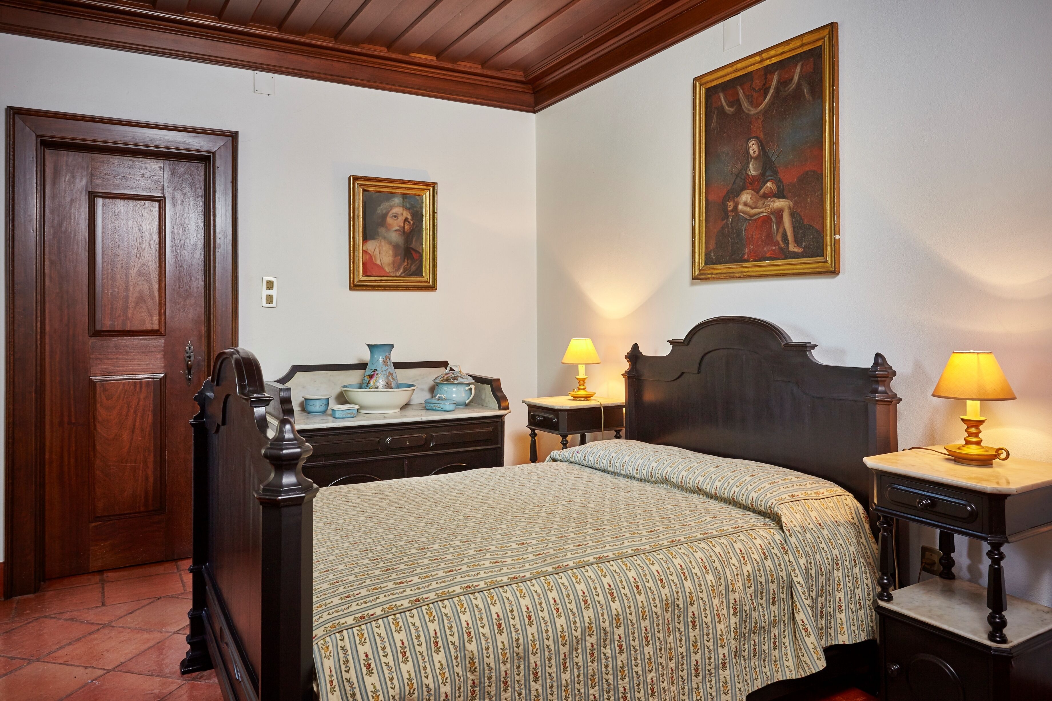 A bedroom with a wooden bed, a dresser, a nightstand, and two wall-mounted lamps.