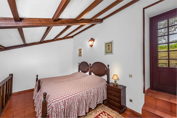 A bedroom with a wooden bed, a nightstand, a wall-mounted lamp, and a door with a view of greenery. - Paço de Calheiros (Ponte de Lima)