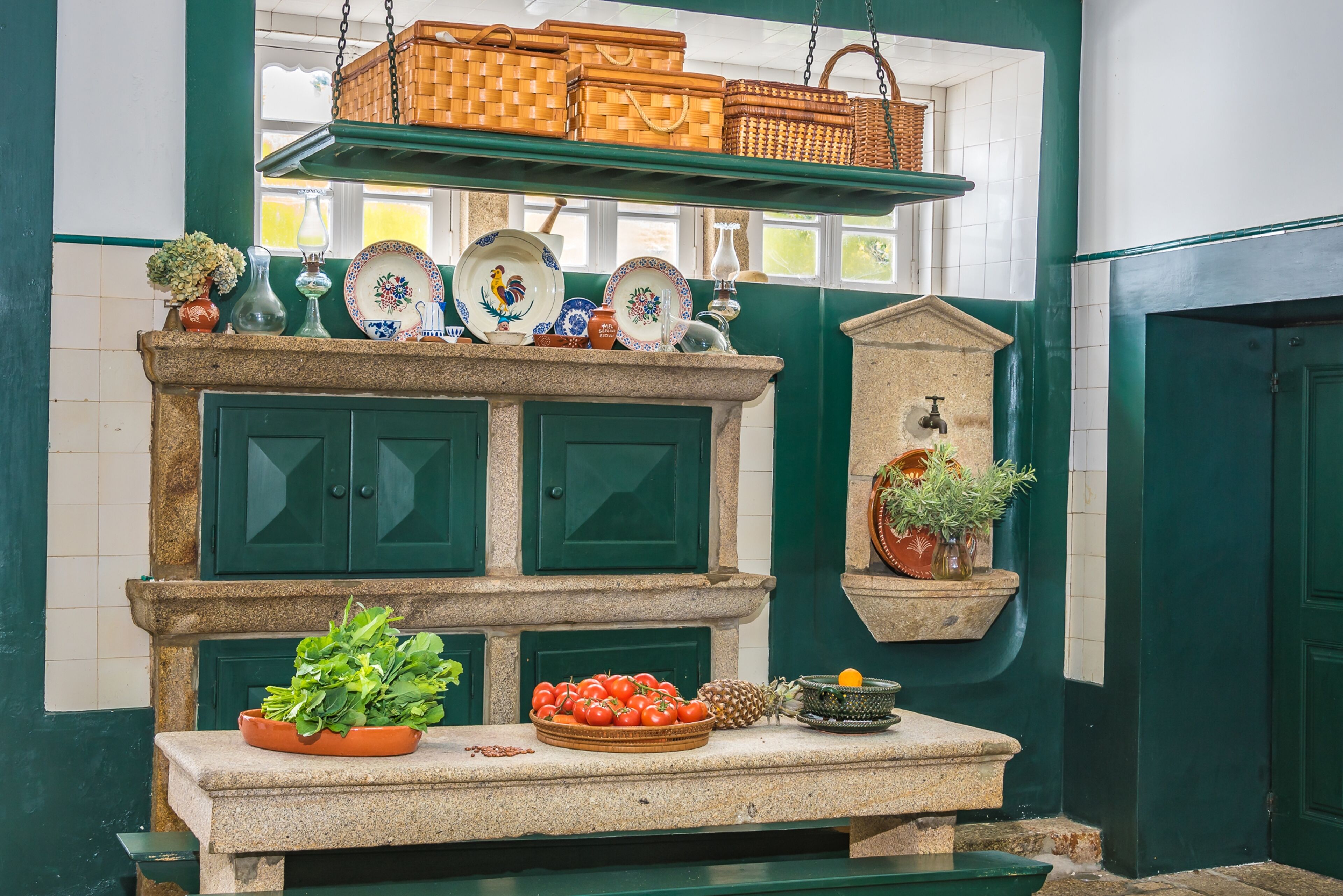 Una cocina con armarios verdes, encimera de piedra y diversos utensilios de cocina y plantas.