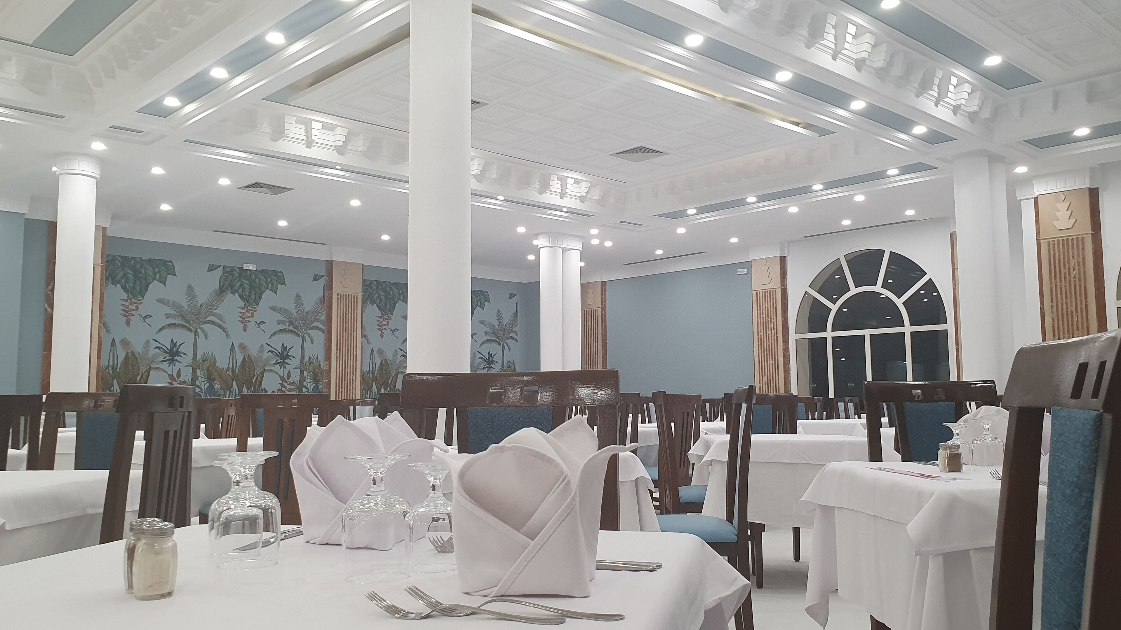 A formal dining area with tables set for service, featuring white tablecloths, glassware, and wooden chairs.