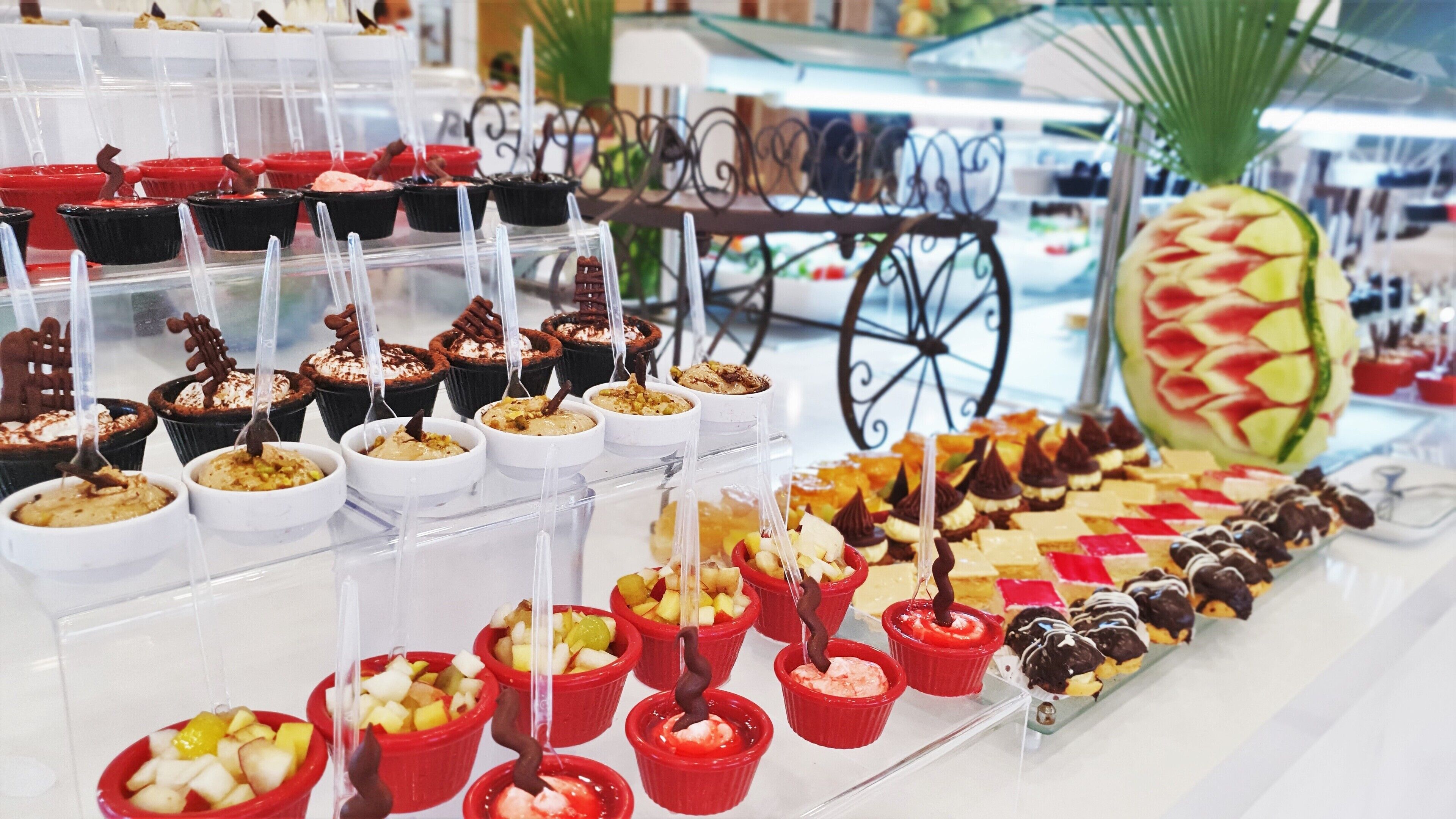 Diverse desserts, zoals cupcakes en desserts op basis van fruit, gepresenteerd in glazen bakken op een toonbank in een winkelomgeving.