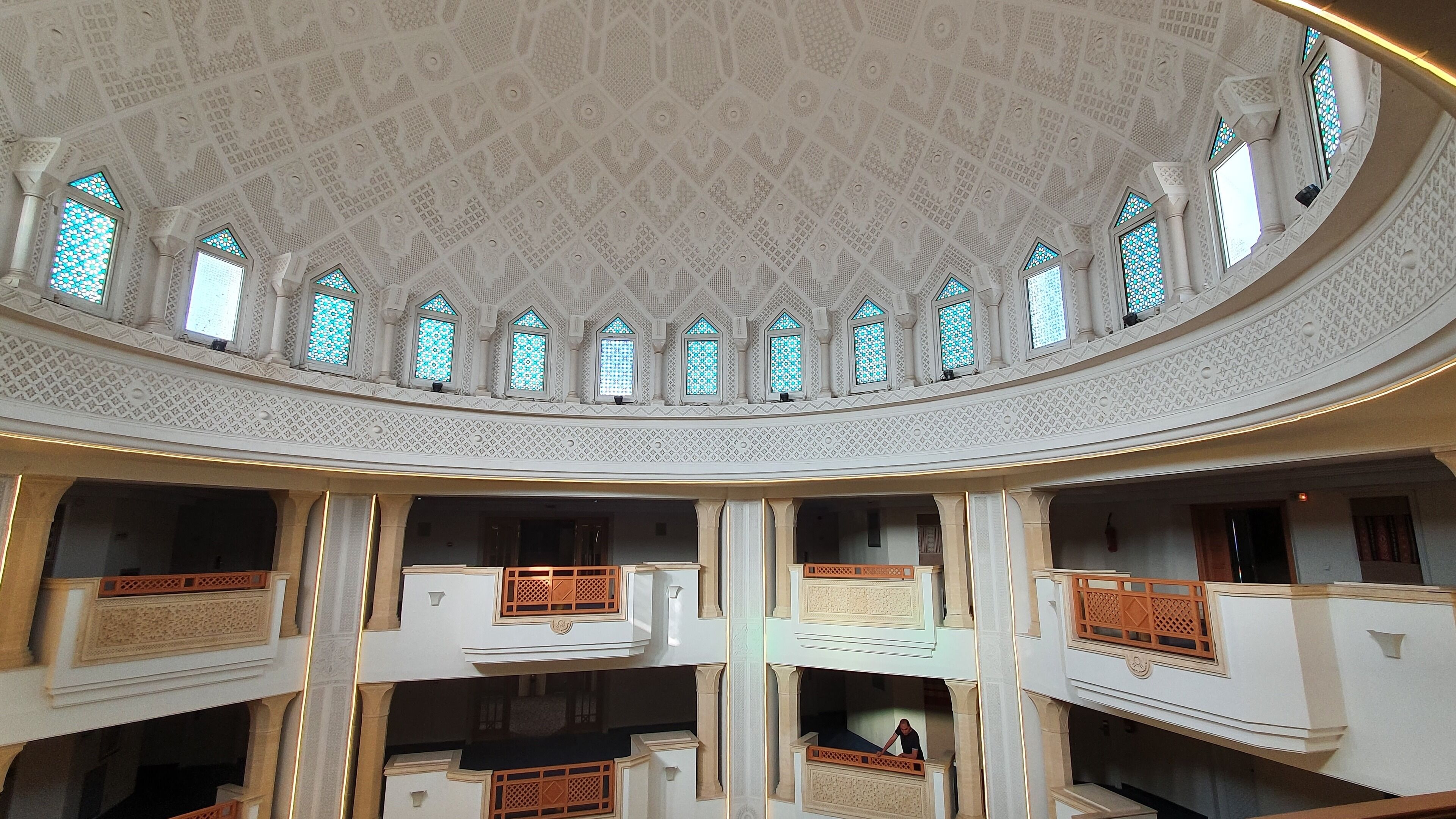 Un atrium à plusieurs niveaux, orné de motifs complexes au plafond et doté de nombreuses fenêtres en arc de cercle.