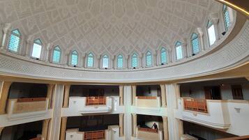 Un atrium à plusieurs niveaux, orné de motifs complexes au plafond et doté de nombreuses fenêtres en arc de cercle.
