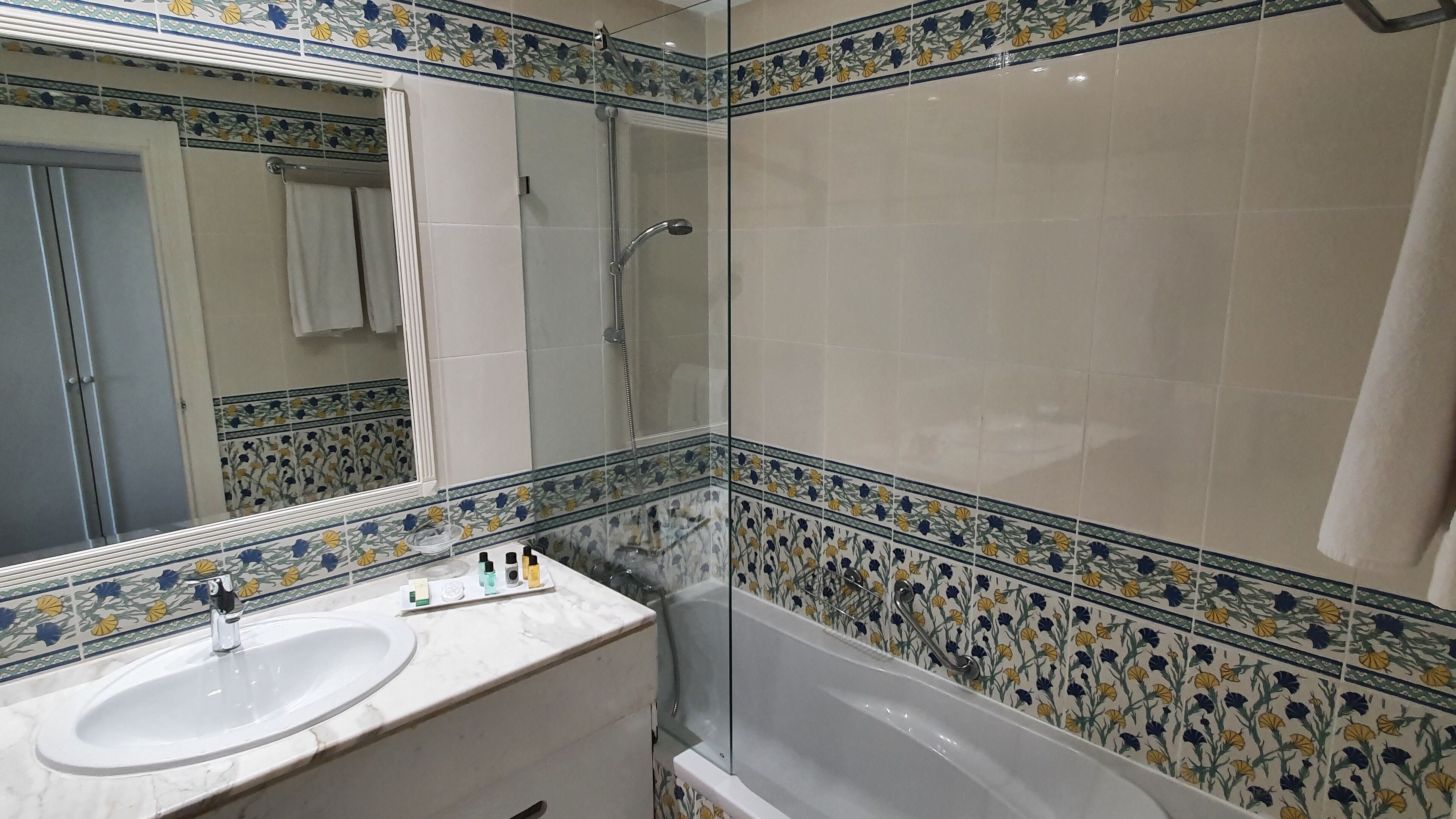 Een badkamer met een wastafel, spiegel, douche en bad.
