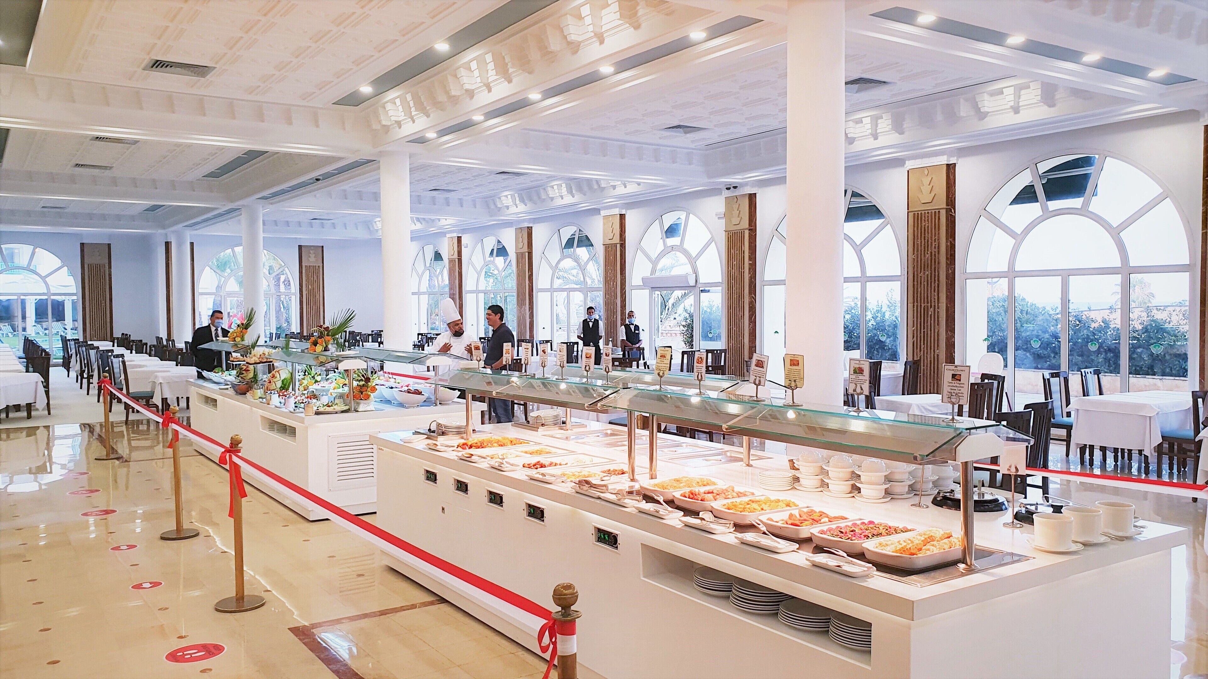 Un buffet bien organisé, avec plusieurs présentoirs de nourriture, un espace propre et spacieux, et de grandes fenêtres laissant entrer la lumière naturelle.