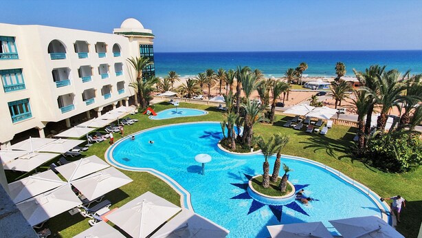 Un resort con una piscina grande, palmeras y vistas al océano.