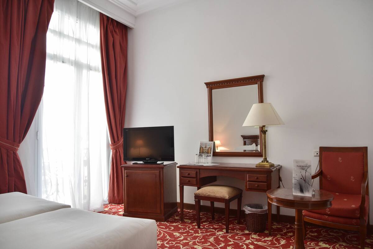 A hotel room with two beds, a desk with a television, a chair, a lamp, and a mirror.
