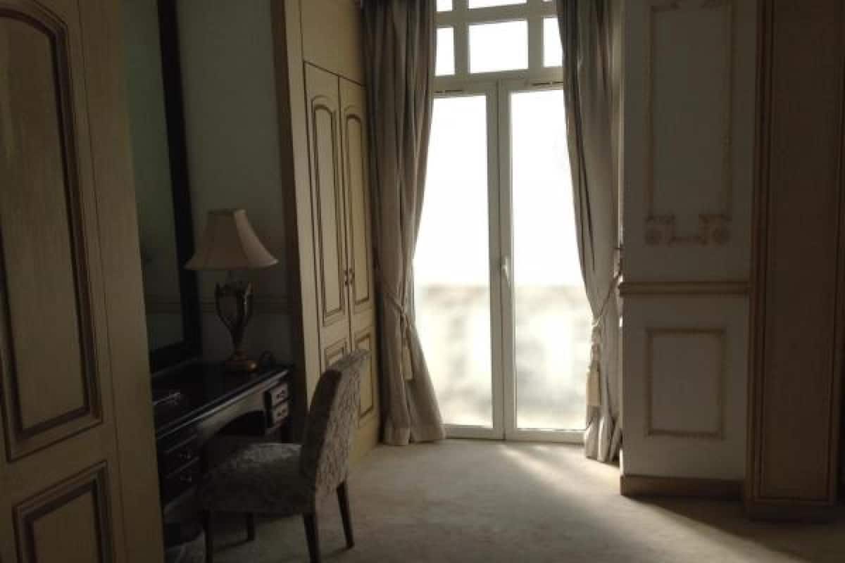 A room with a desk, chair, and a large window with curtains.