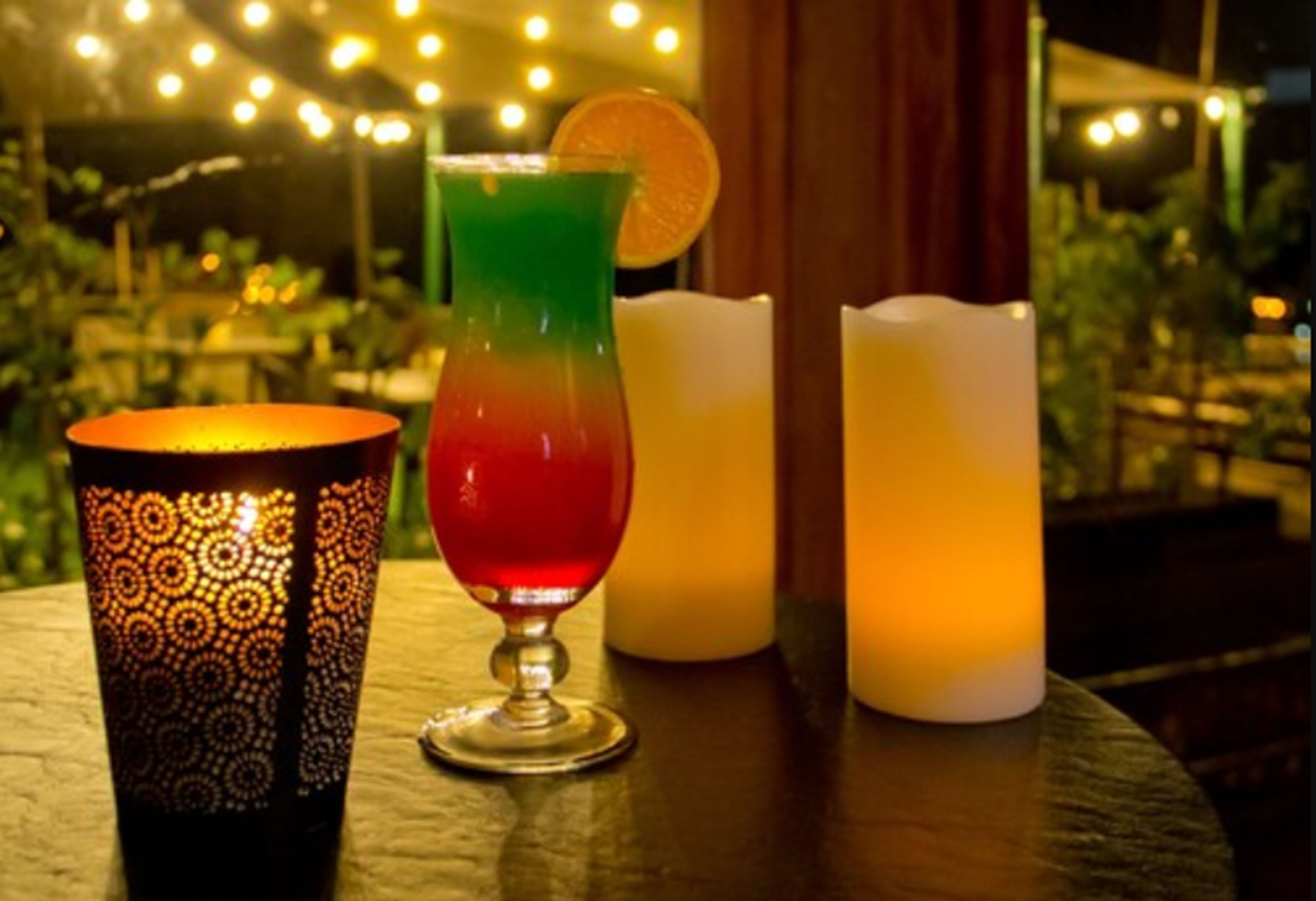 A table with a patterned glass, a colorful drink, and two candles.