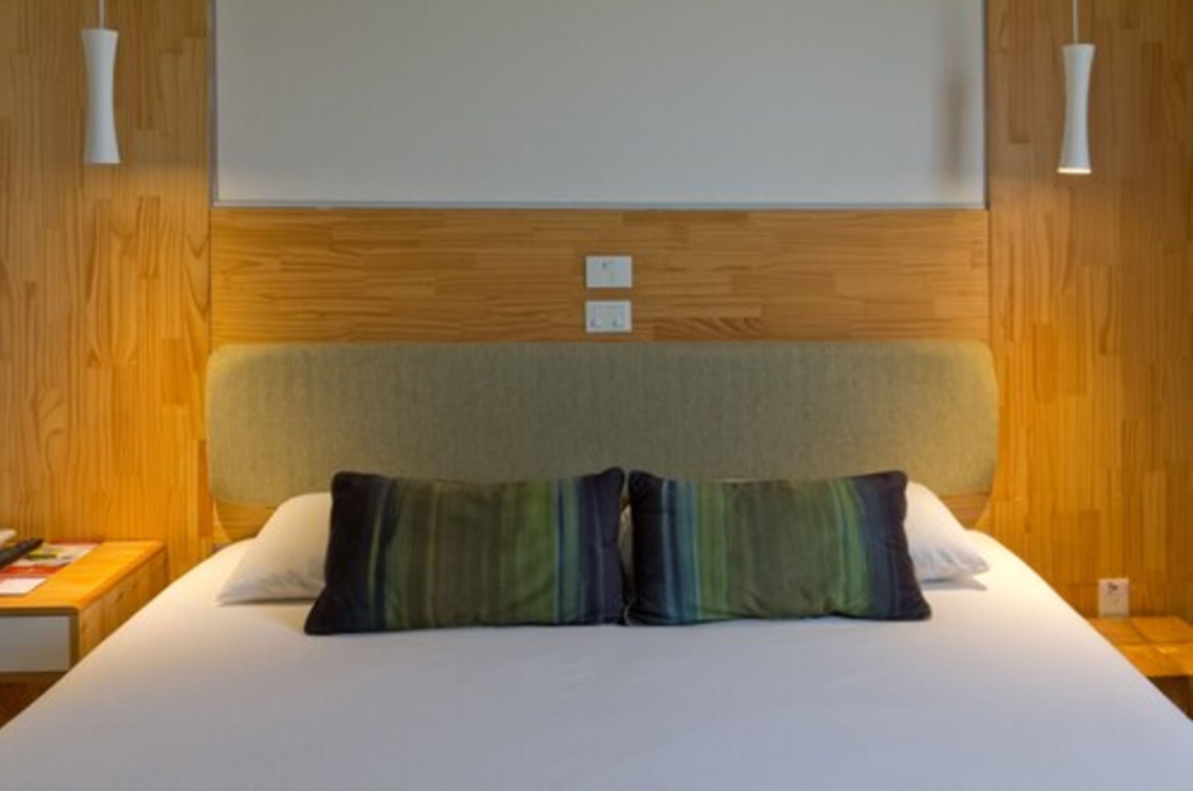 Una habitación de hotel con cabecera de madera, dos almohadas, una mesita de noche y un tocador.