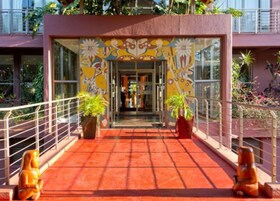 Entrada de hotel con un mural colorido, plantas en macetas y un suelo de baldosas rojas.