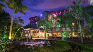 A hotel with a water feature in front, palm trees, and illuminated balconies. - Amérian Portal del Iguazú Hotel (Puerto Iguazú)
