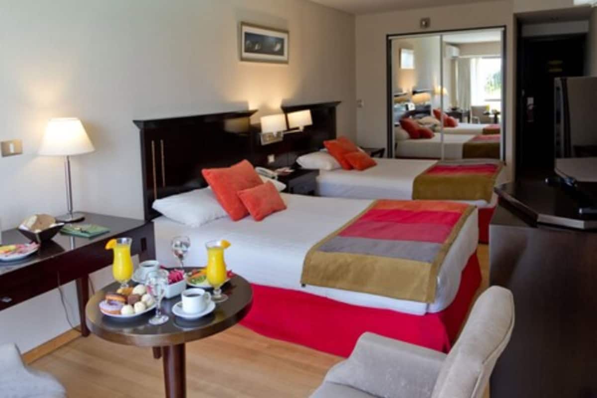 Une chambre d’hôtel avec deux lits, un bureau avec des articles pour le petit-déjeuner, une chaise et un miroir.