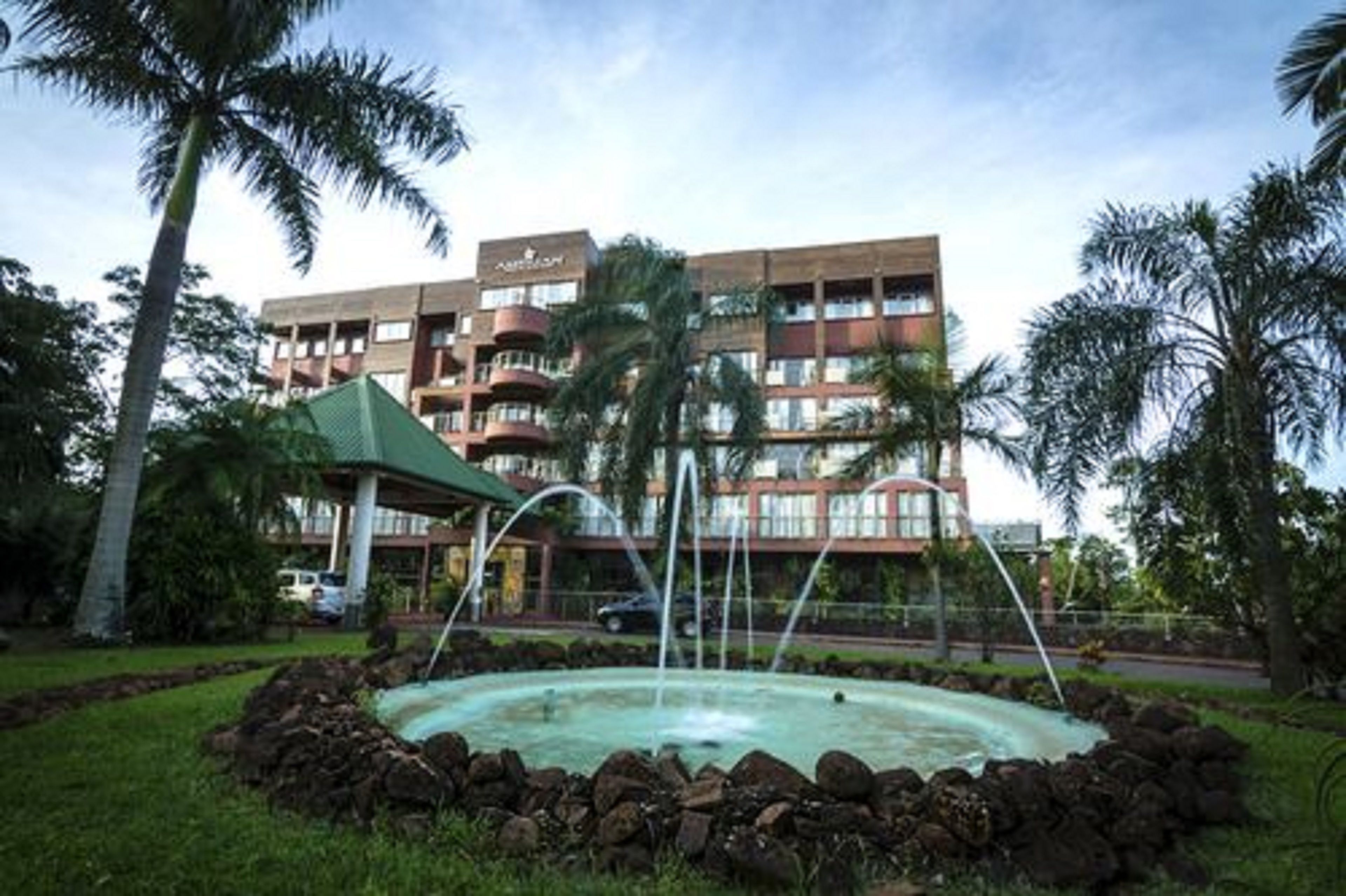 A hotel with a swimming pool, palm trees, and a covered pavilion.