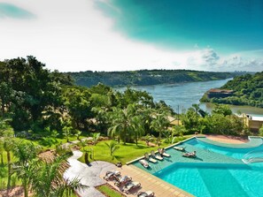 A pool area with lounge chairs, a clear view of a river, and lush greenery. - Amérian Portal del Iguazú Hotel (Puerto Iguazú)