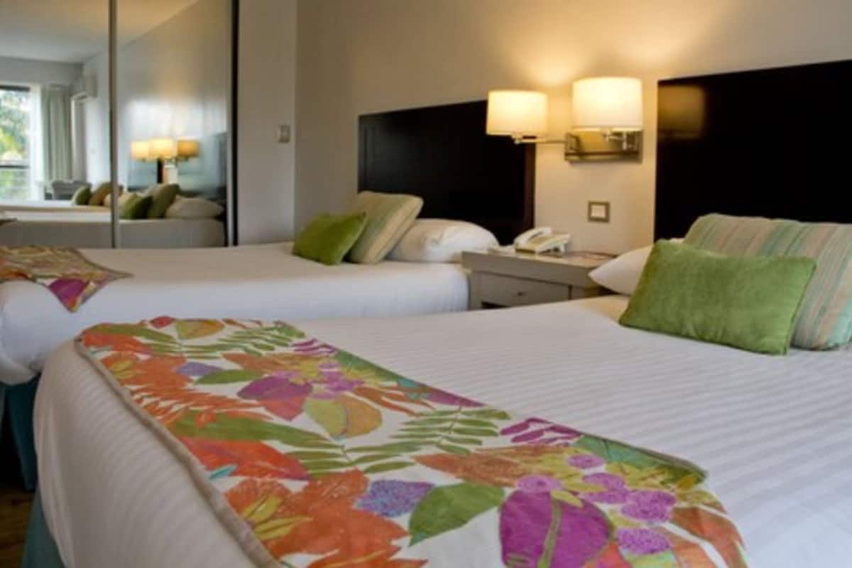 Une chambre d’hôtel avec deux lits, chacun recouvert d’une couvre-lit à motifs floraux, une table de chevet avec une lampe et un miroir au mur.