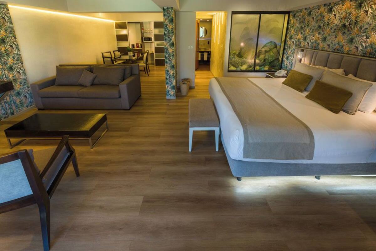 Une chambre d’hôtel moderne avec un grand lit, un canapé, une table basse et un coin repas à l’arrière-plan.