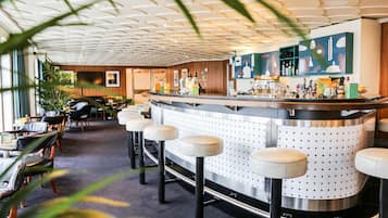 Eine Bar mit Hockern, einer Theke und einer Decke mit geometrischem Muster.