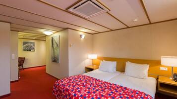 Ett hotellrum med en stor säng, två sängbord med lampor, ett rött heltäckningsmatta, en träpanel vid sänggaveln och en inramad tavla på väggen.