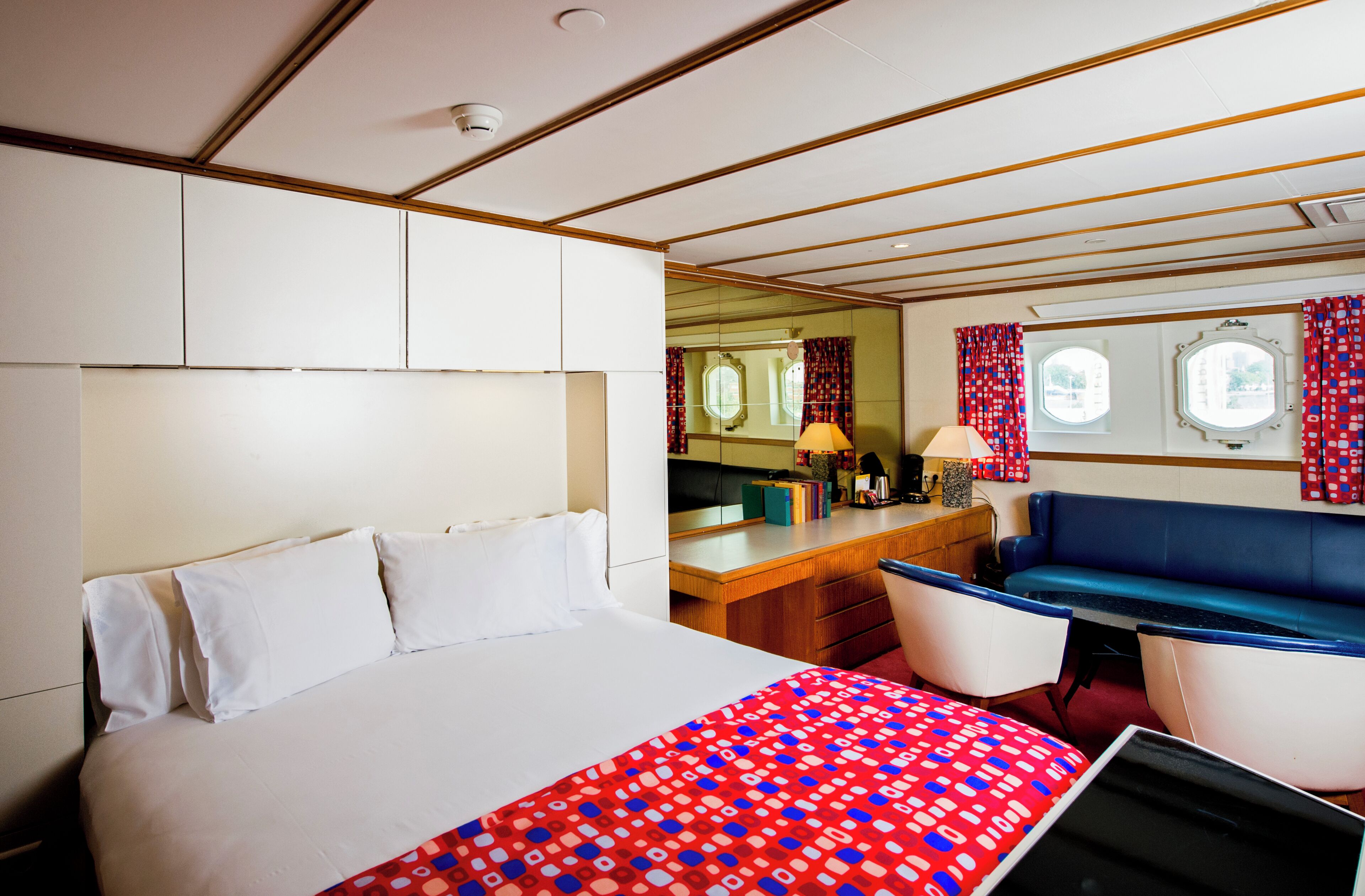 A hotel room with a large bed, a desk with a lamp, a blue sofa, and a window with curtains.