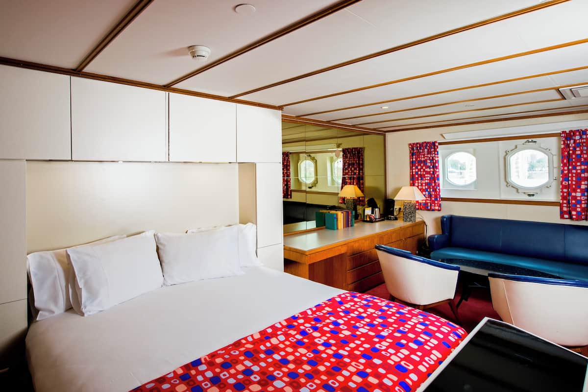 A hotel room with a large bed, a desk with a lamp, a blue sofa, and a window with curtains.
