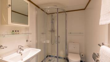 Un baño con ducha envuelta en vidrio, un lavamanos blanco y un inodoro.