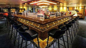 Un espace bar doté d’un bar central, de nombreux tabourets et d’un plafond bien éclairé.