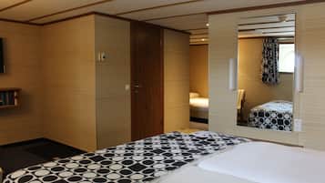 Ein Schlafzimmer mit einem Bett, einem Kleiderschrank, einem Spiegel und einem kleinen Regal mit Büchern.