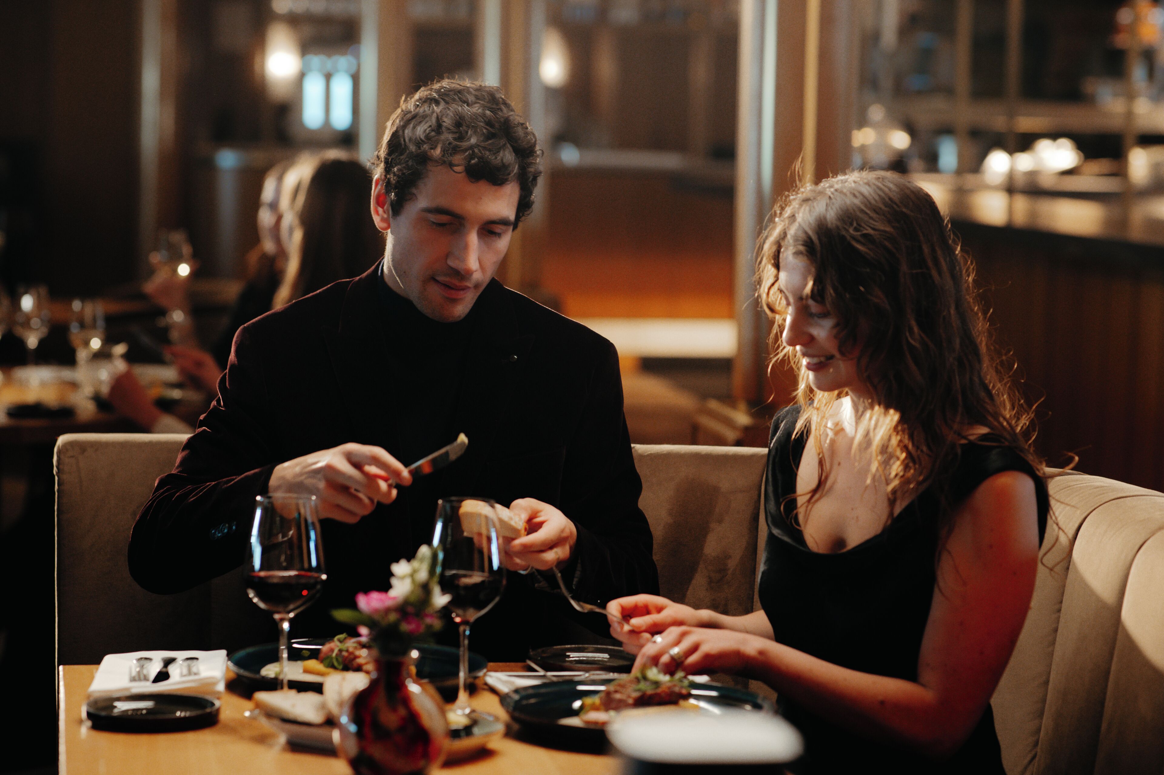 A couple dining at a restaurant with a table set for two, wine glasses, and a menu.