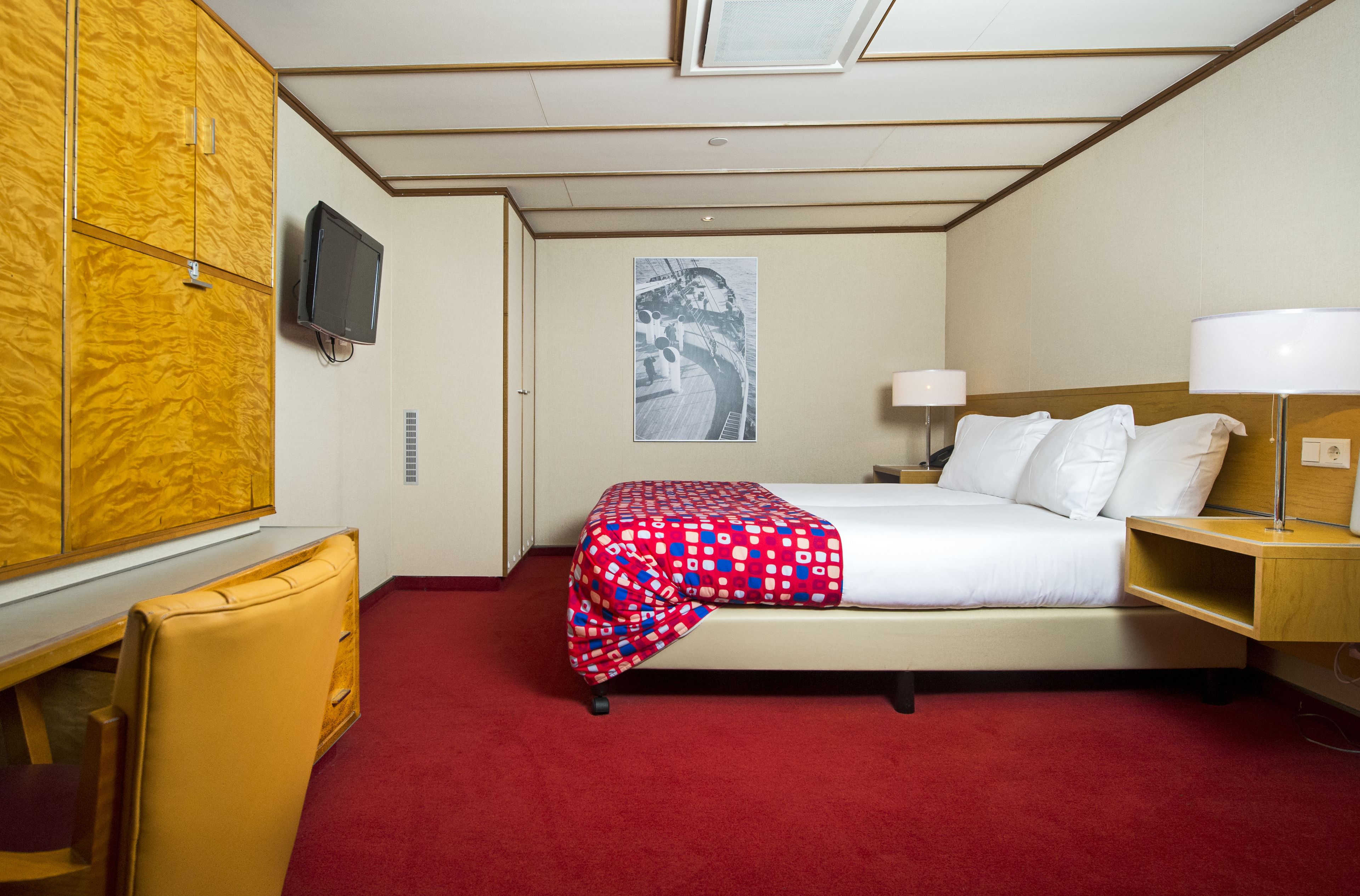 A hotel room with a bed, a desk, a chair, a television, and a window.