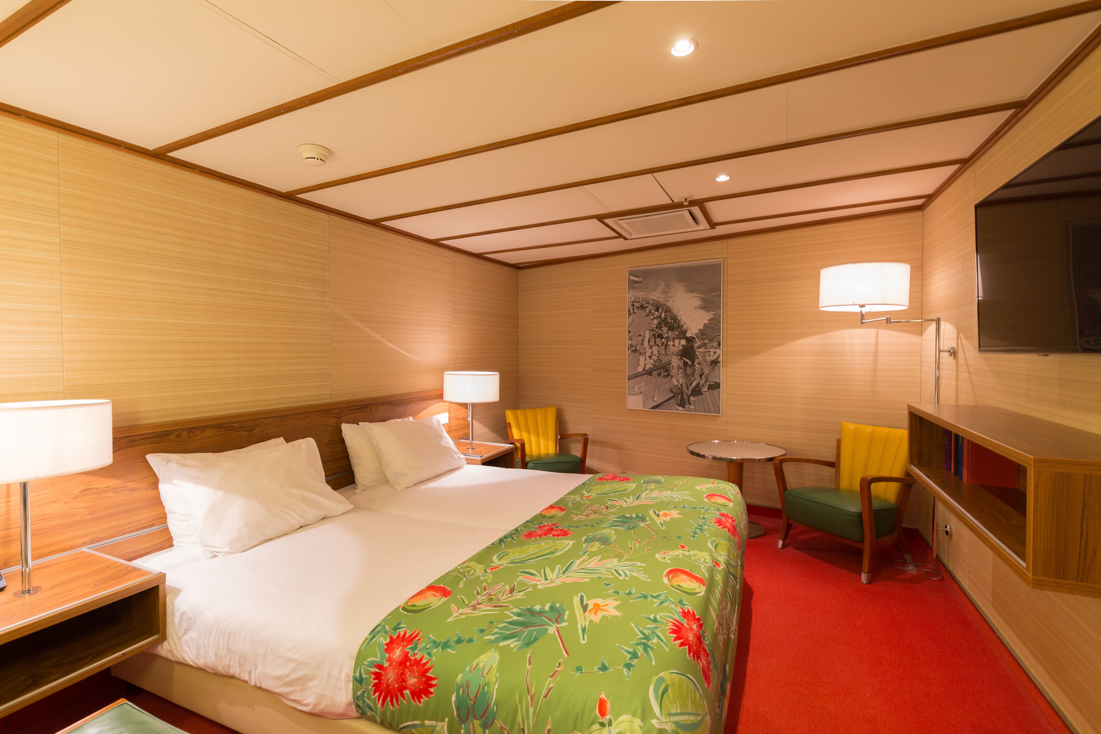 Een hotelkamer met een bed, twee stoelen, een klein tafeltje en een televisie.