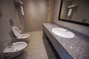 Et moderne badeværelse med to toiletter, en vask med granitbordplade og et stort spejl.