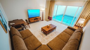 Een woonkamer met een grote bank, een salontafel, een televisie en een balkon met uitzicht op zee.
