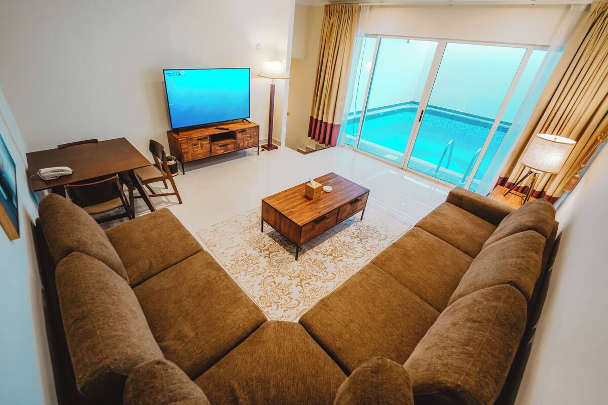Een woonkamer met een grote bank, een salontafel, een televisie en een balkon met uitzicht op zee.