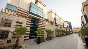 Een modern gebouw met een stenen gevel, grote ramen en palmbomen langs het pad.