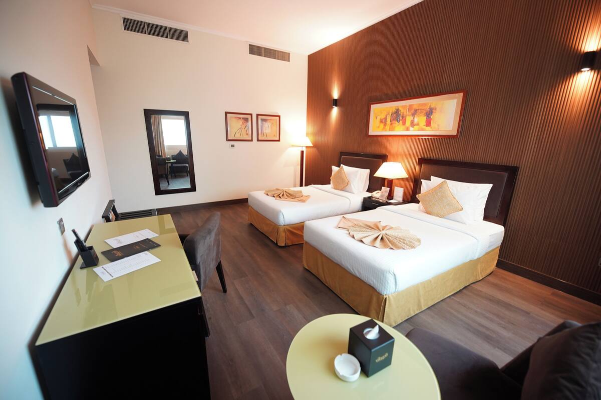 Hotelkamer met twee bedden, een bureau, een stoel, een tafel met een doos en een televisie aan de muur.