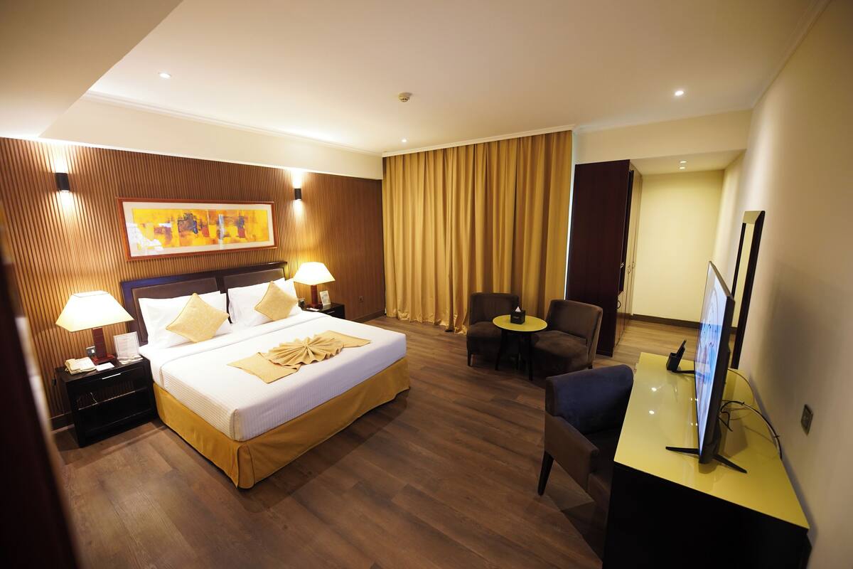Een hotelkamer met een bed, nachtkastjes, een bureau, een stoel, een televisie en een schilderij aan de wand.
