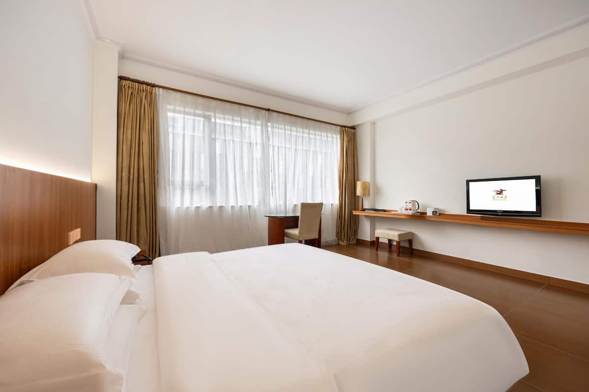 A hotel room with a large bed, a desk, a chair, a television, and a window with curtains.