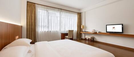 A hotel room with a large bed, a desk, a chair, a television, and a window with curtains.