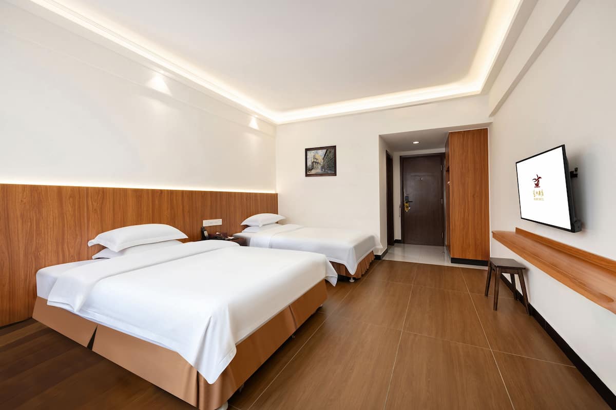 A hotel room with two beds, a wooden headboard, a flat-screen TV, a small table, and a door leading to another room.