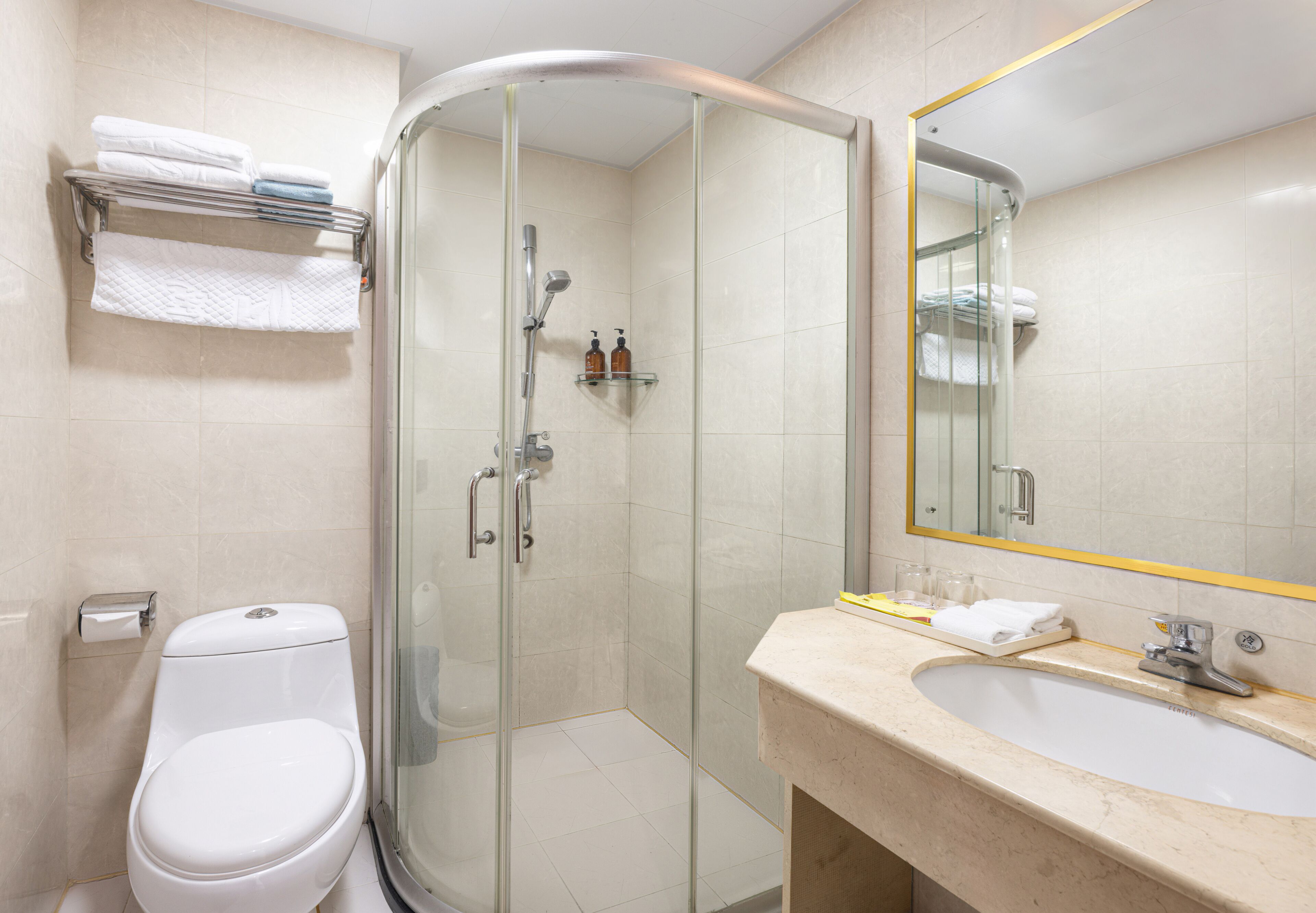 A modern bathroom with a glass shower enclosure, a toilet, a sink with a mirror, and neatly arranged towels.