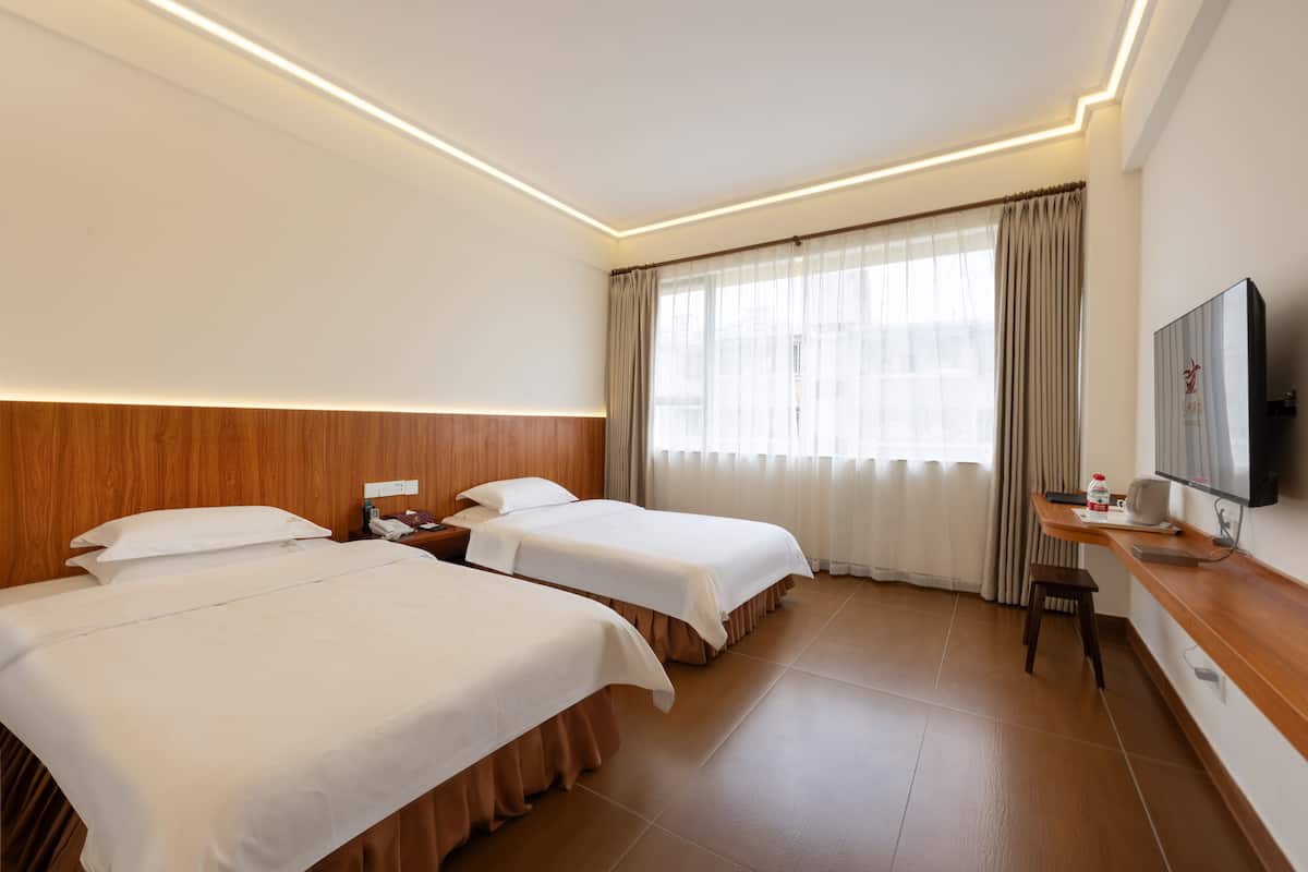 A hotel room with two beds, a desk with a chair, a TV, and a window with curtains.