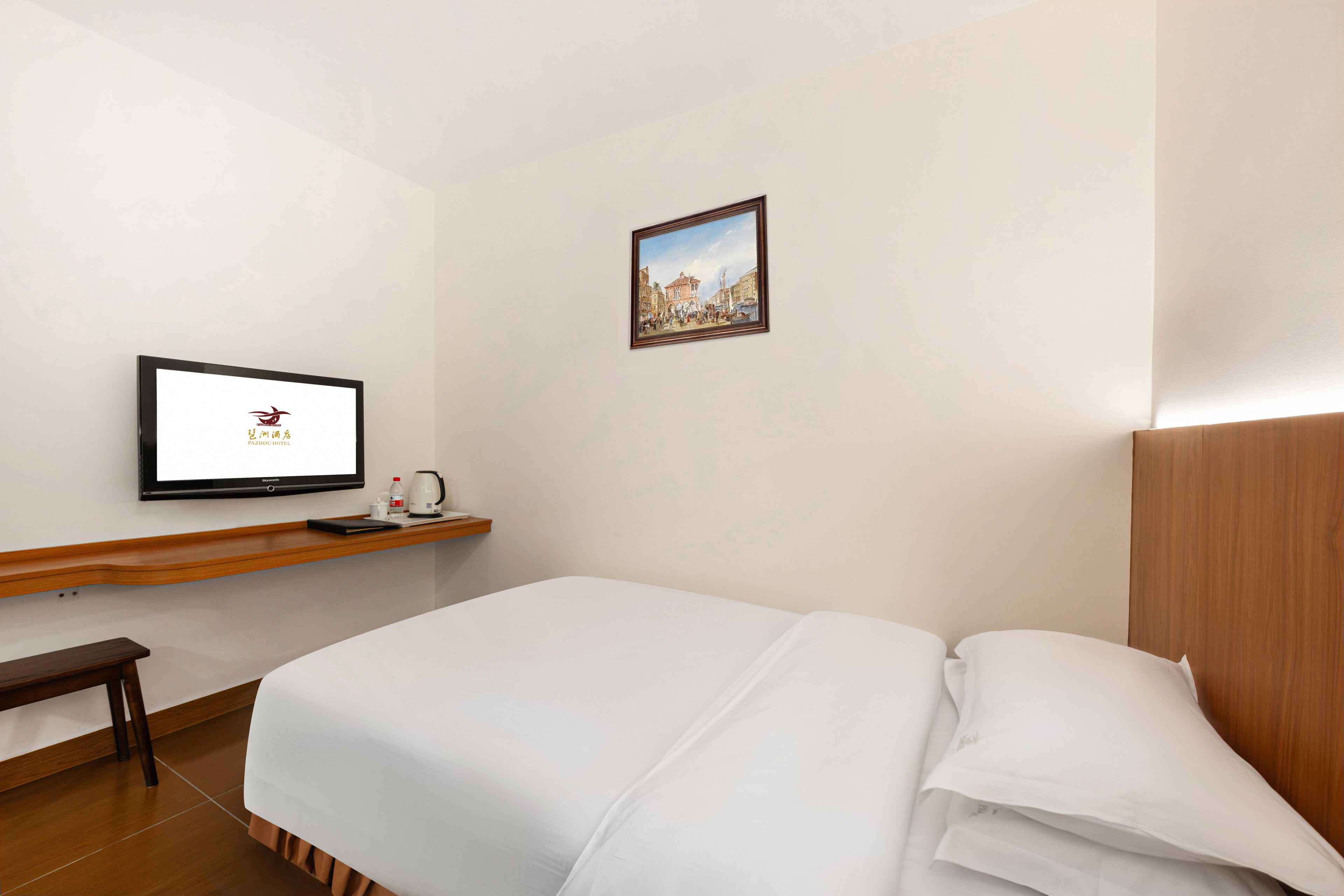Une chambre d’hôtel avec un lit, un téléviseur posé sur un meuble, une petite table avec une bouilloire et un tableau encadré accroché au mur.