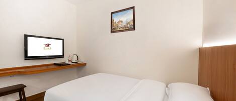 Une chambre d’hôtel avec un lit, un téléviseur posé sur un meuble, une petite table avec une bouilloire et un tableau encadré accroché au mur.