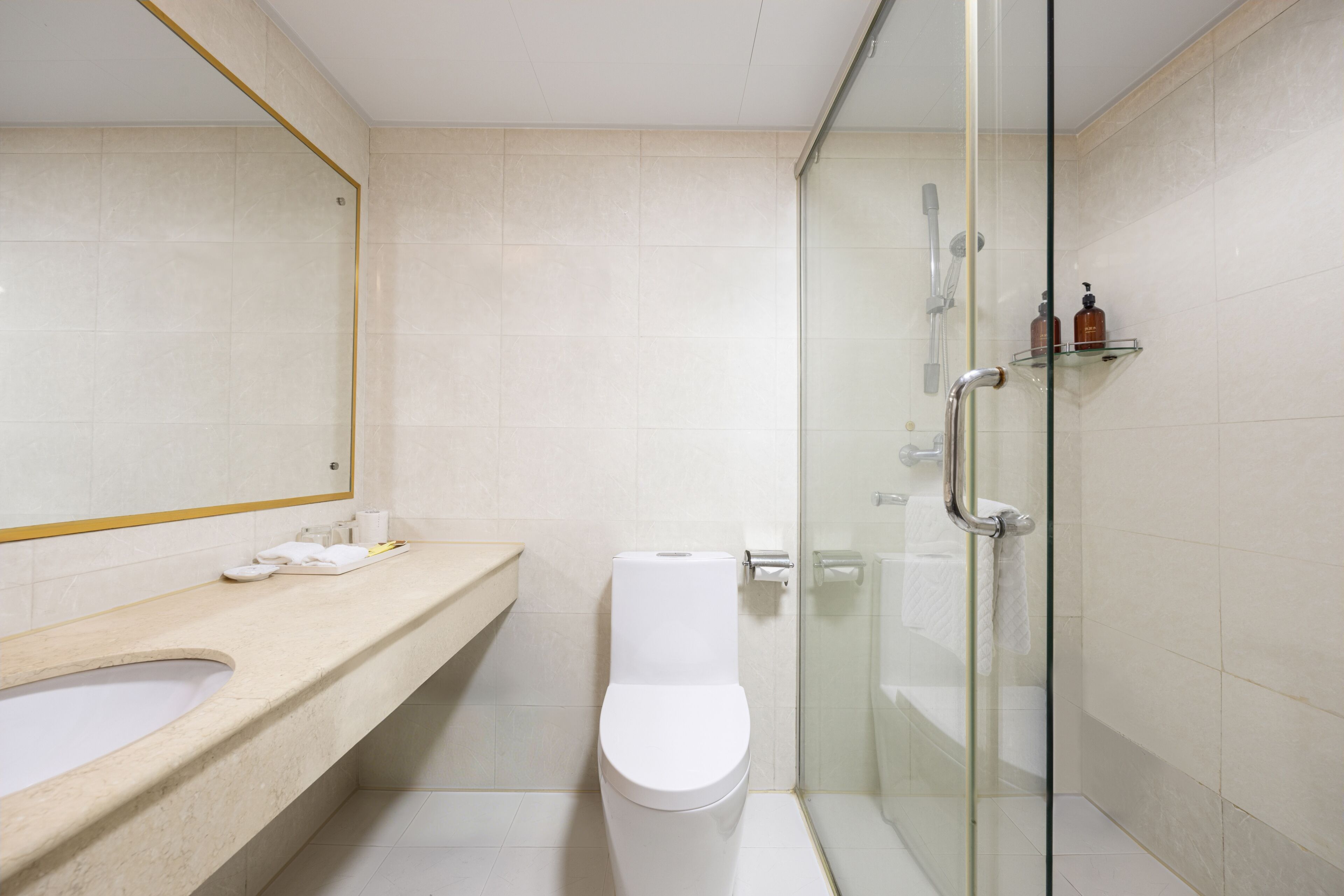 Une salle de bain moderne avec une douche à parois de verre, des toilettes blanches et un meuble-lavabo beige agrémenté d’un miroir.