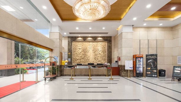 A hotel lobby with a reception desk, a chandelier, a marble wall, and a vending machine. - Pazhou Hotel (Guangzhou)